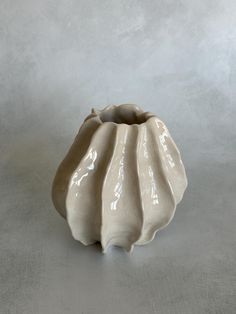 a white ceramic vase sitting on top of a table next to a gray wall and floor