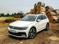 a white volkswagen tigua is parked in front of some large rocks and hay bales