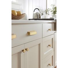 a kitchen with white cabinets and gold pulls on the handles, along with a bowl of fruit