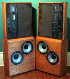 two wooden speakers sitting side by side on top of a hard wood floor next to a green wall