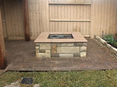 a brick fire pit sitting in the middle of a yard next to a wooden fence