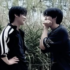 two young men standing next to each other in front of some tall grass and plants