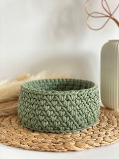 a green crocheted bowl sitting on top of a woven mat next to a vase