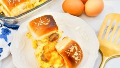 two breakfast sandwiches sitting on top of a white plate next to an egg and cheese casserole