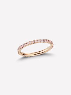 a gold ring with pink stones on the side and a thin band around it, in front of a white background