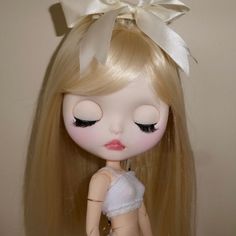 a close up of a doll with long blonde hair and big eyes wearing a white dress