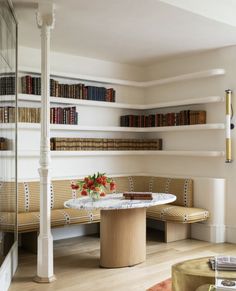 a room with bookshelves and a table in the center, surrounded by wooden benches