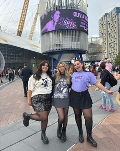 three girls are posing for the camera in front of a building with a giant sign on it