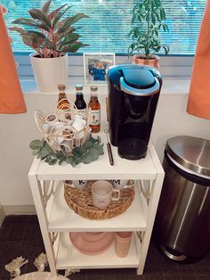 a coffee maker and other items sit on a small table next to a trash can