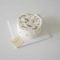 a white cake with daisies on it sitting on top of a piece of paper