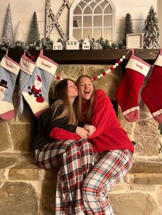 two women sitting on a fireplace with christmas stockings hanging from the mantel above them