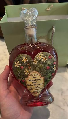 a hand holding a heart shaped bottle in front of a box with flowers on it