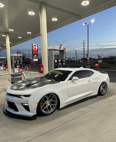 a white chevrolet camaro is parked at a gas station