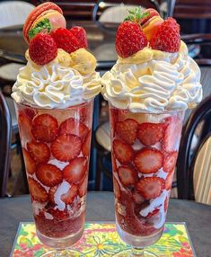 two cups filled with whipped cream and strawberries on top of a table next to each other