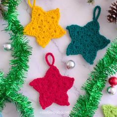 crocheted ornaments and pine cones on a white table with christmas tree decorations in the background