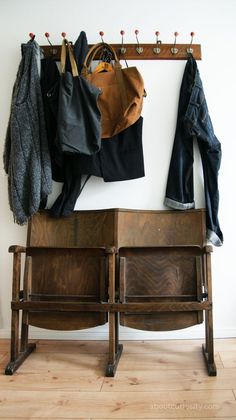 an old wooden bench with clothes hanging on it's back and coat rack above