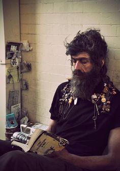 a man with long hair and beard sitting down reading a book