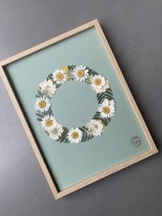 a frame with flowers on it sitting on a table next to a wall mounted painting