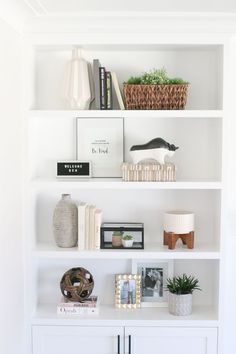 a white book shelf filled with books next to a lamp and pictures on the wall