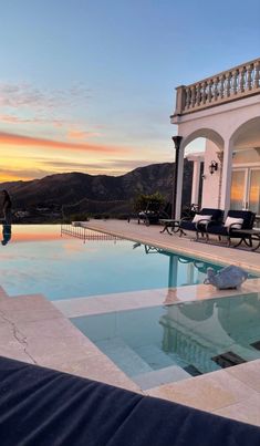 a large swimming pool in front of a white house with mountains in the background at sunset