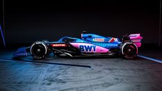 a pink and blue race car on display in a dark room with lights behind it