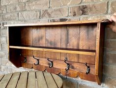 a wooden coat rack with four hooks on it and a bench in front of a brick wall