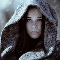 a young woman is wrapped up in a gray hoodie and looking at the camera