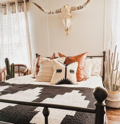 a black and white bed topped with lots of pillows next to a wall mounted cow skull