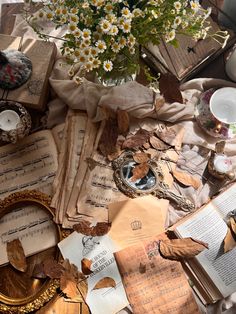 a table topped with lots of old books and papers next to a vase filled with flowers