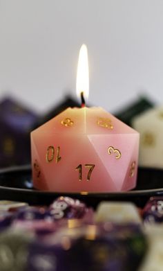 a pink dice sitting on top of a black plate next to some dices and a candle