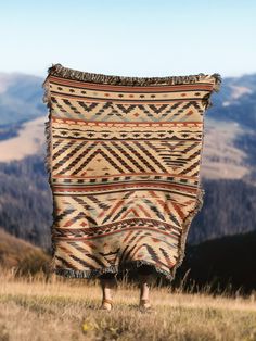 a person standing on top of a grass covered hill holding a blanket over their head