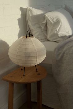 a white lamp sitting on top of a wooden table next to a bed with pillows