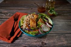 a salad in a blue bowl on top of a wooden table next to a fork