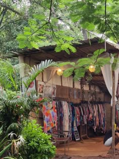 an outdoor clothing store with clothes hanging from the roof and trees in front of it