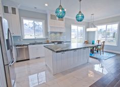 a large kitchen with marble counter tops and white cabinets, two pendant lights hanging from the ceiling