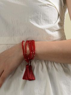 a woman wearing a white dress with red beads and a tassel on her arm