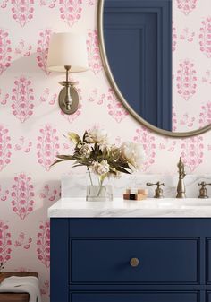 a bathroom vanity with blue cabinets and pink wallpaper