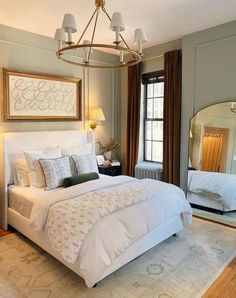 a large white bed sitting under a chandelier in a bedroom next to a window