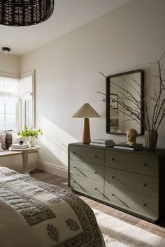 a bedroom with a dresser, mirror and lamp in it's corner next to a window