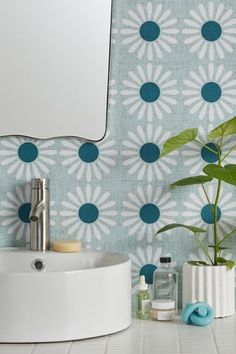 a white sink sitting under a bathroom mirror next to a green leafy wallpaper