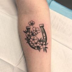 a black and white photo of a flowered horseshoe tattoo on the right leg, with flowers in it