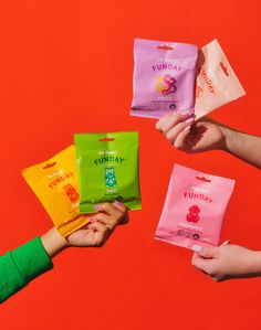 four people are holding colorful candy bags in their hands on an orange and red background