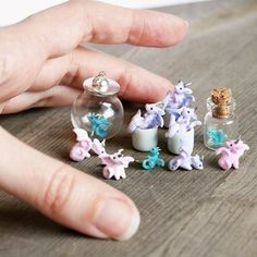 someone is holding their hand over some tiny figurines in a glass bottle on the table