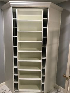 an empty white bookcase in the corner of a room with marble floors and walls