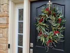 a wreath on the front door of a house with pine cones and berries hanging from it