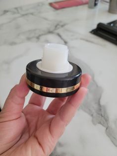 a hand holding an electronic device in front of a marble counter top with makeup products on it