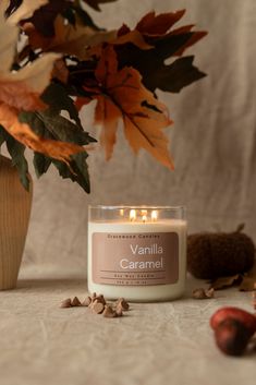 a candle sitting on top of a table next to leaves and acorns in a vase