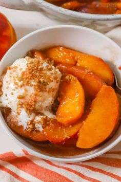 a bowl filled with peaches and cream on top of a striped table cloth next to an apple