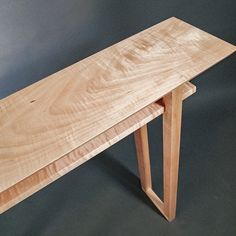 a wooden bench sitting on top of a gray floor next to a white wall and black background