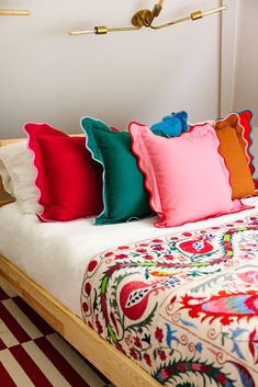 a bed with colorful pillows on top of it in front of a white wall and checkered floor